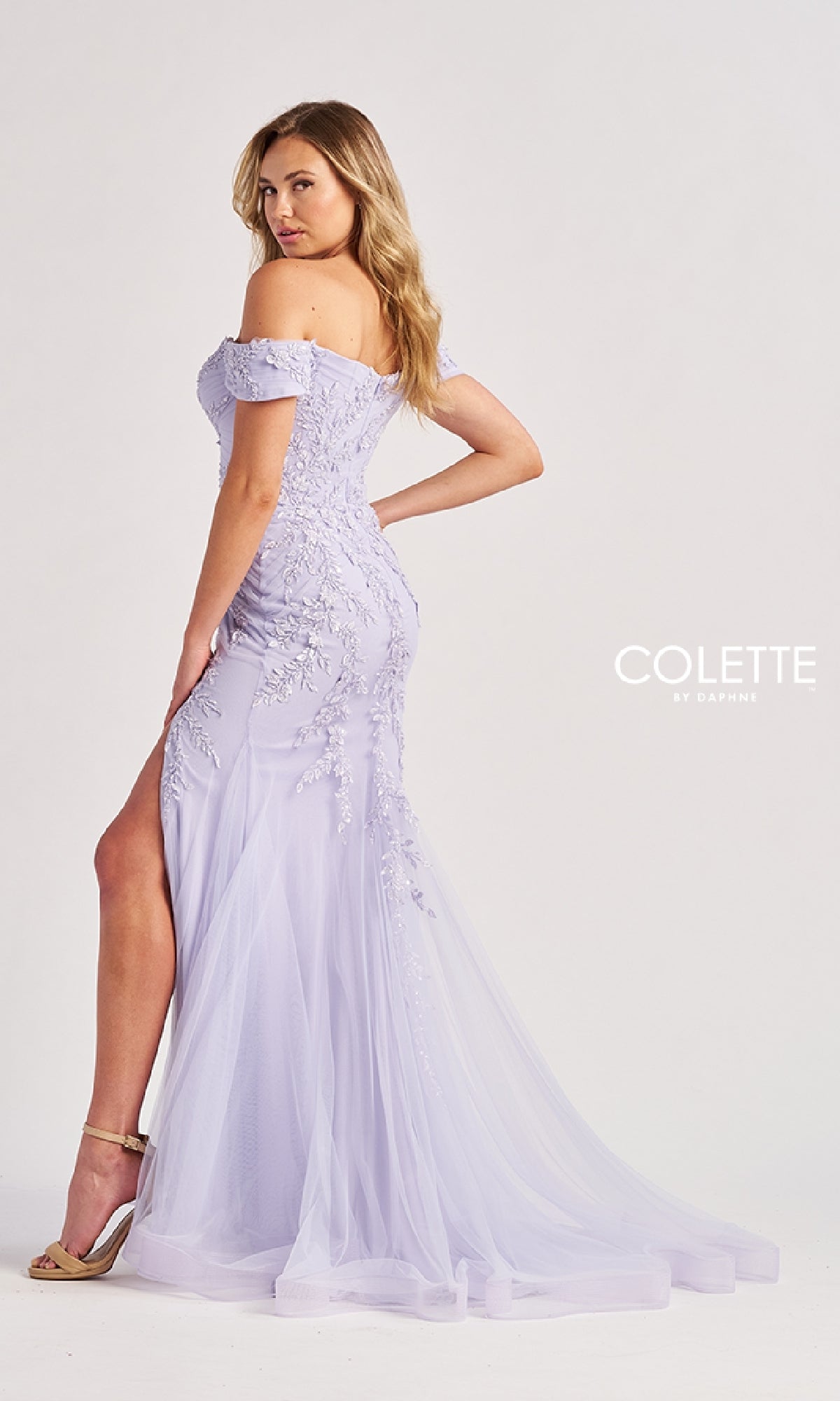 A woman stands in profile against a plain background, wearing the Off-the-Shoulder Long Prom Dress Colette CL8645—a light lavender gown with beaded floral details, high slit, sheer train, and off-the-shoulder design.